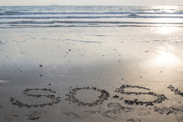 SOS big written on the beach by the sea.