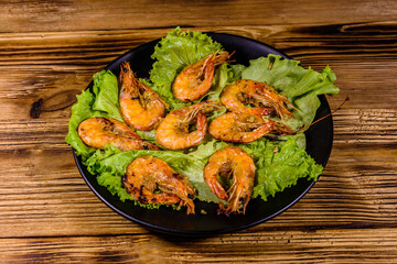 Plate with grilled shrimps and lettuce leaves on a wooden table