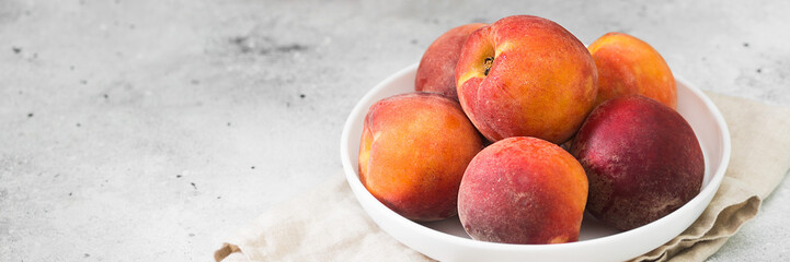 Peaches in a white plate on the light gray kitchen table. Red ripe peaches on a plate. Banner with space for text