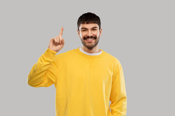 count and people concept - smiling young man in yellow sweatshirt showing one finger over grey background