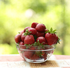 strawberry in bowl close up vertical photo with copy space on green grass background