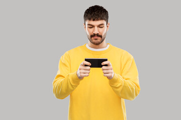 technology, communication and people concept - young man playing game on smartphone over grey background