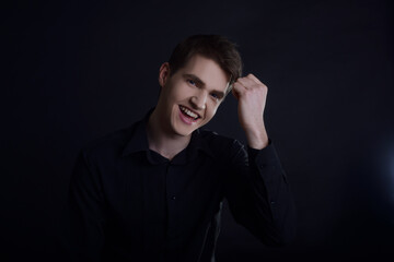 Studio portrait of a guy in a black shirt on a black background. A handsome young guy of European appearance. The guy laughs, the guy in a good mood looks at the camera