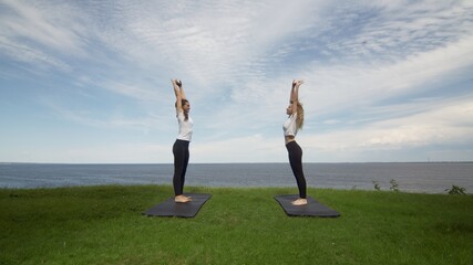 Fototapeta na wymiar Two young women practicing meditation and yoga in nature at high mountain cliff near the sea.