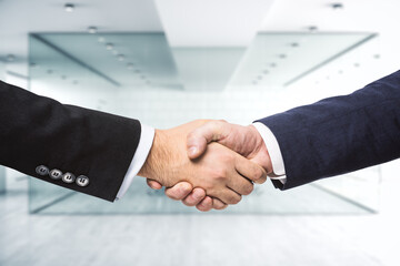 Two businessmen shake hands on the background of sunny modern furnished office, deal concept, close up