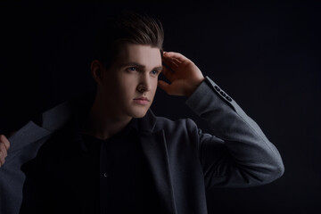 Studio portrait of a man with a raincoat on a black background. Muddy with a perfect hairstyle, European appearance posing, model in the side light. Personal care