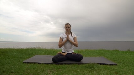 Fototapeta na wymiar Young fit woman practice yoga on coast near the lake or sea. Woman sitting in Knee Pile pose and meditating