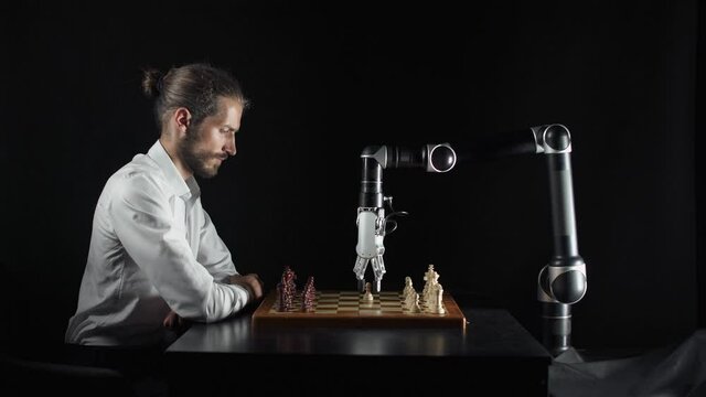 Modern technology, man playing chess with a robot, the confrontation between man and artificial intelligence, futuristic robotic arm participates in the game.