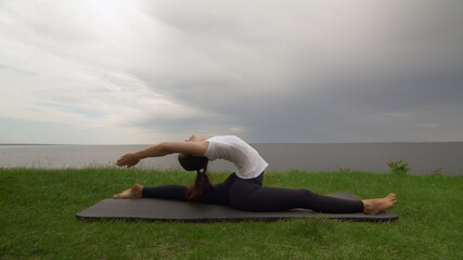 Young fit woman practice yoga on coast near the lake or sea. Woman sitting in Front Splits Hanumanasana pose