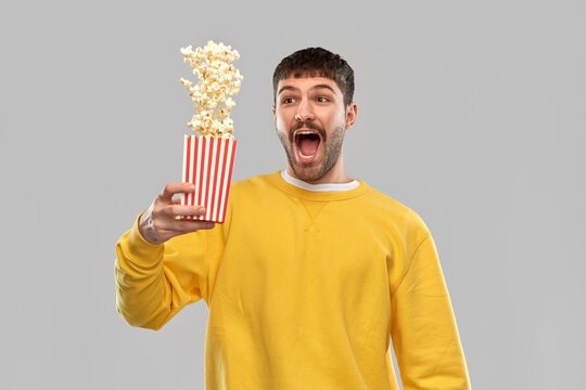 fast food and people concept - happy young man in yellow sweatshirt playing with popcorn over grey background