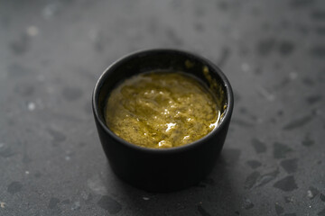 Olive oil with mustard and spices in small black bowl on concrete background