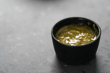 Olive oil with mustard and spices in small black bowl on concrete background