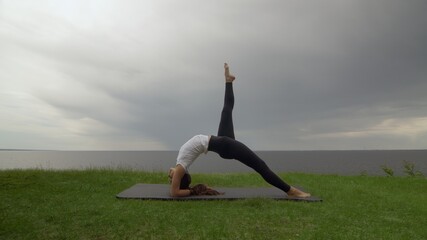 Young fit woman practice yoga on coast near the lake or sea. Woman doing Inverted Staff Dvi Pada Viparita Dandasana pose