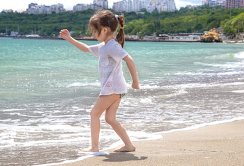 Little cute girl runs on a Sunny day on the beach by the sea