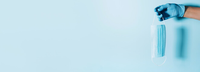 Hand with blue medical gloves holding medical facemask on background. Banner with copy space. Health protection equipment during quarantine Coronavirus pandemic. Stay safe. Covid 19