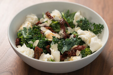 Salad with kale, sun-dried tomatoes and mozzarella in white bowl