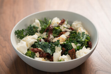 Salad with kale, sun-dried tomatoes and mozzarella in white bowl