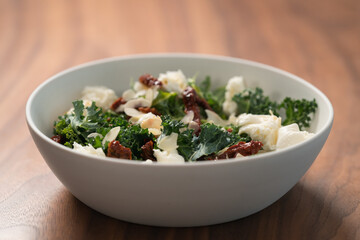 Salad with kale, sun-dried tomatoes and mozzarella in white bowl