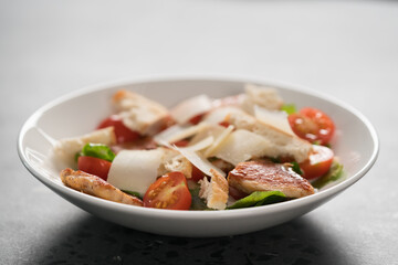 Fresh caesar salad with chicken and cherry tomatoes in white bowl