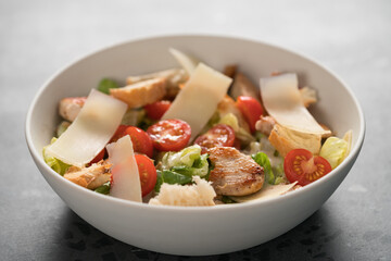 Fresh caesar salad with chicken and cherry tomatoes in white bowl