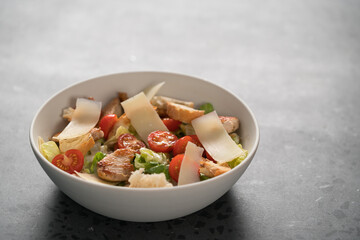 Fresh caesar salad with chicken and cherry tomatoes in white bowl