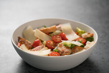 Fresh caesar salad with chicken and cherry tomatoes in white bowl