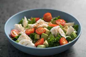 Salad with avocado, mozzarella, tomatoes and kale in blue ceramic bowl