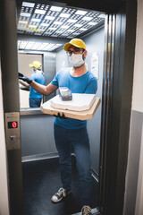 Deliveryman with protective medical mask holding pizza box and POS wireless terminal for card paying - days of viruses and pandemic, food delivery to your home.