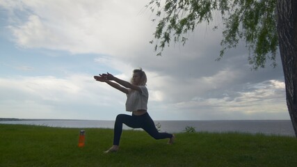 Young fit woman practice yoga on coast near the lake or sea. Woman doing Warrior I Pose