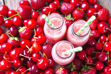 Summer smoothies in a glass bottles on a red berries background