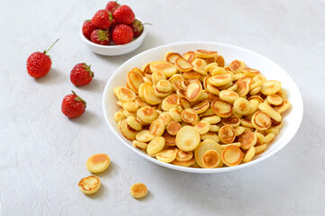 Pancake cereal in a bowl with fresh strawberries on a light background. Tasty and trendy breakfast. Organic Dutch Mini-Pancakes. Foods trend