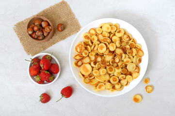Pancake cereal in a bowl with fresh strawberries and nuts on a light background. Tasty and trendy breakfast. Organic Dutch Mini-Pancakes.