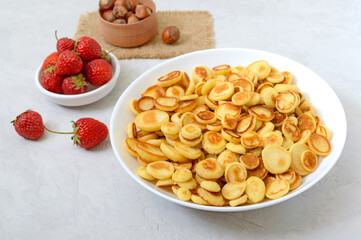 Pancake cereal in a bowl with fresh strawberries and nuts on a light background. Tasty and trendy breakfast. Organic Dutch Mini-Pancakes.