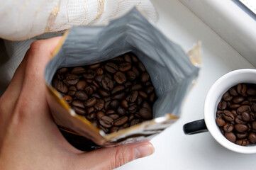 Hand holds an open package of coffee beans.