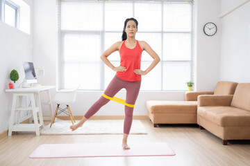 Fototapeta premium Asian woman exercising at home on a yoga mat. She uses rubber resistance.