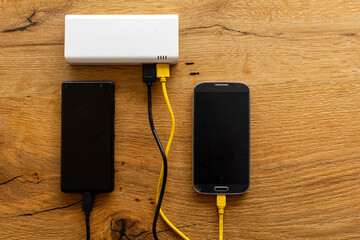 Two Mobile Phone sharing USB Power Bank on a wooden Table to charge the mobile devices