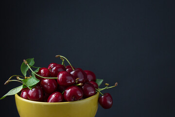 A bowl ful of red cherries on black background with space for text