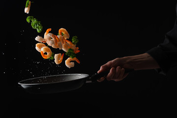 Shrimps with parsley frying in a pan, the chef cooks, freezing in motion on a black background, healthy and tasty food