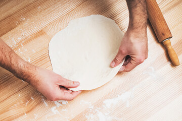 Man's hands working with dough on wooden table,