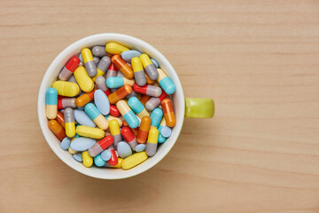 Cup colorful tablets and capsules on wooden background. Health care concept