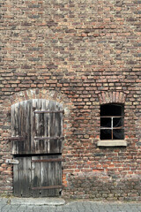 Fototapeta na wymiar small wooden old door and window without glass in an abandoned house of old brick, tourist, historical concept, gloomy architecture of European cities