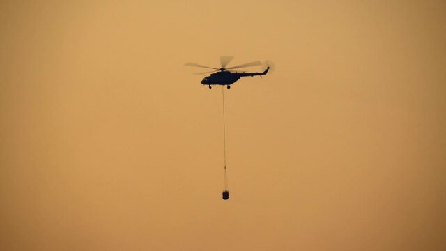 Silhouette Fire fighting helicopter carry water bucket for forest fire