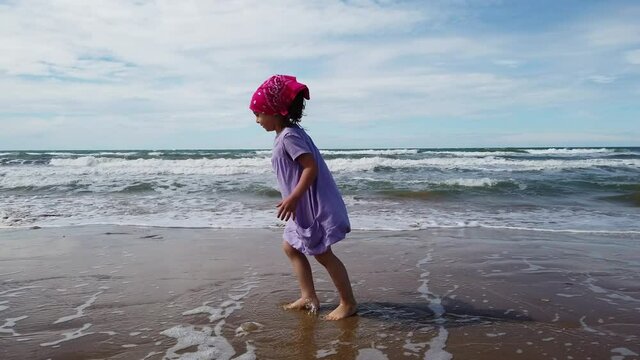 child on ad the sea beach with rough sea have fun walking and jumping with a bandana and purple dress