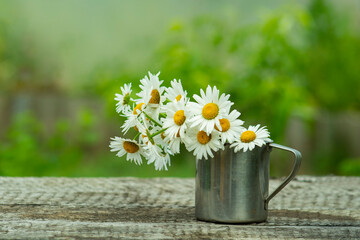 Old metal mug with a bouquet of daisies.