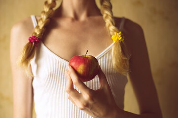 Red apple in a female hand. Young girl with pigtails in a white top.