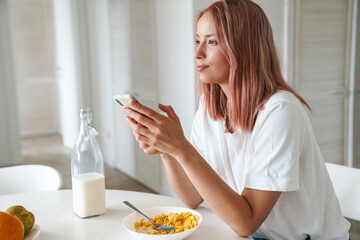 Obraz na płótnie Canvas Photo of young caucasian woman using cellphone while having breakfast