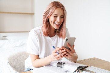 Image of woman using smartphone while doing homework with exercise books