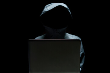 Portrait of Invisible man in the hood on black background. Hacker with laptop.