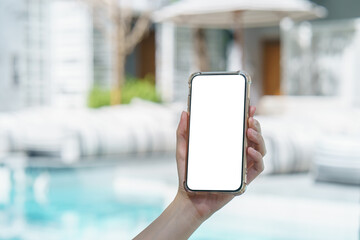 Woman hand holding blank white screen mobile phone near swimming  pool.