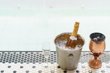 Champagne bottle in ice bucket and two glasses near jacuzzi pool.